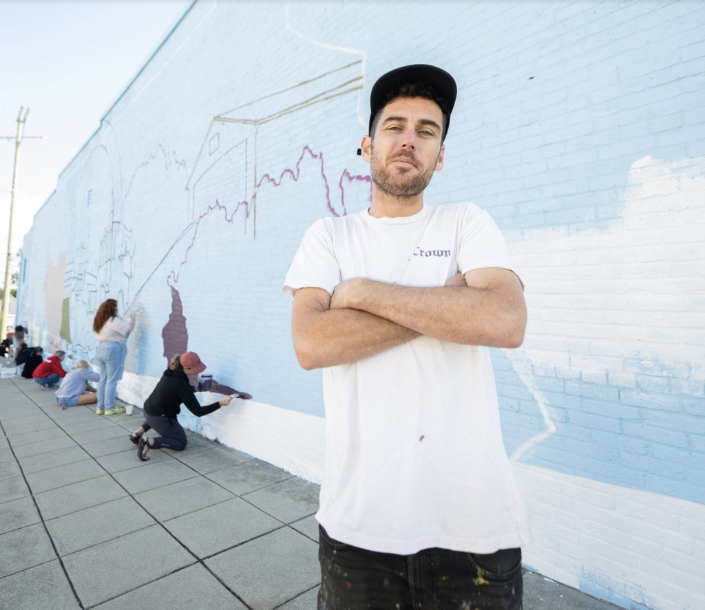 A man in a white t-shirt standing in front of people painting a mural